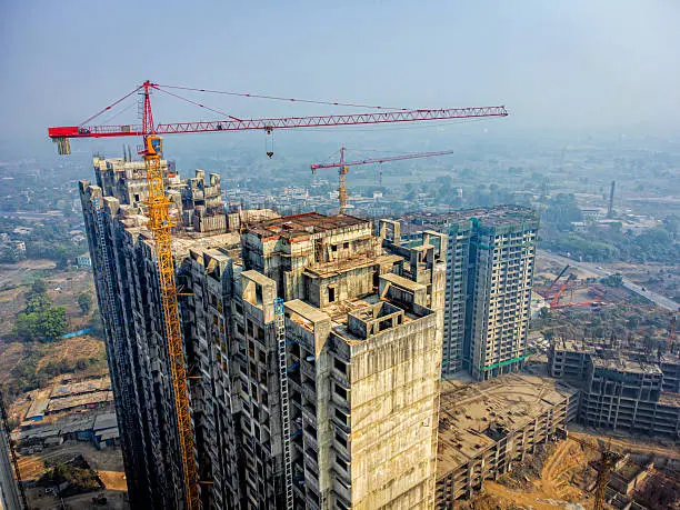 A tower crane mounted over an under construction high rise apartment building in the backdrop of rural Panvel, Navi Mumbai, Maharashtra, India
